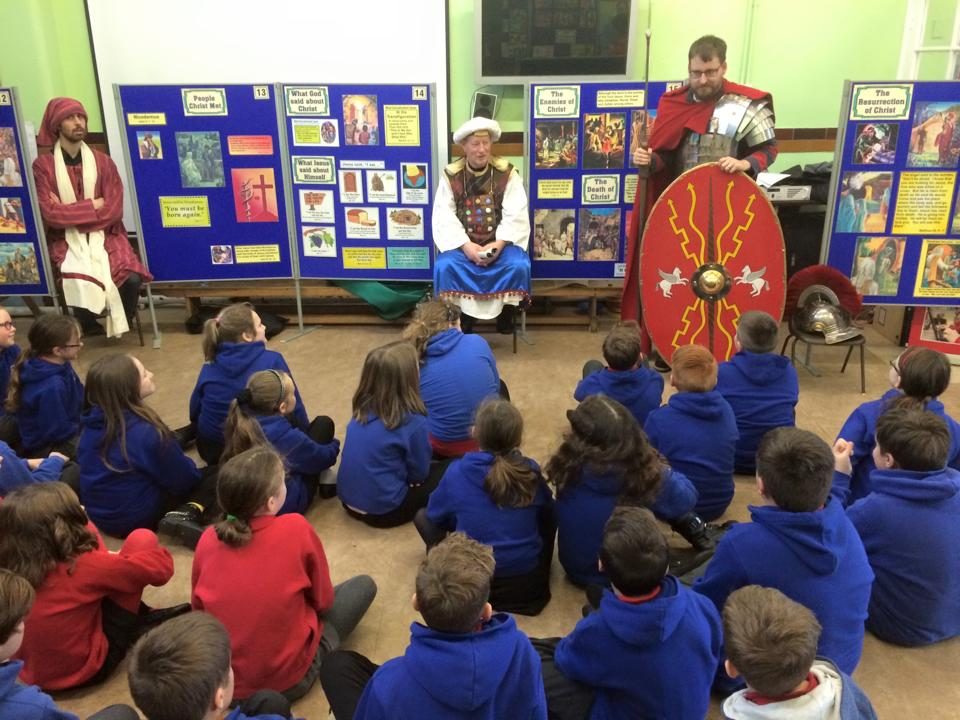 Pupils sitting on the floor listening to costumed narrators in front of the exhibition boards